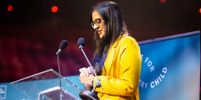 Fozia Nisar speaking at the Theatre for Every Child launch event. She is wearing a bright yellow blazer.