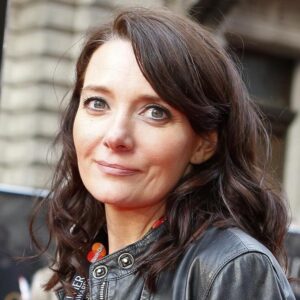 Emma De Souza - curled brunette hair, wearing a leather jacket and Olivier Awards lanyard.